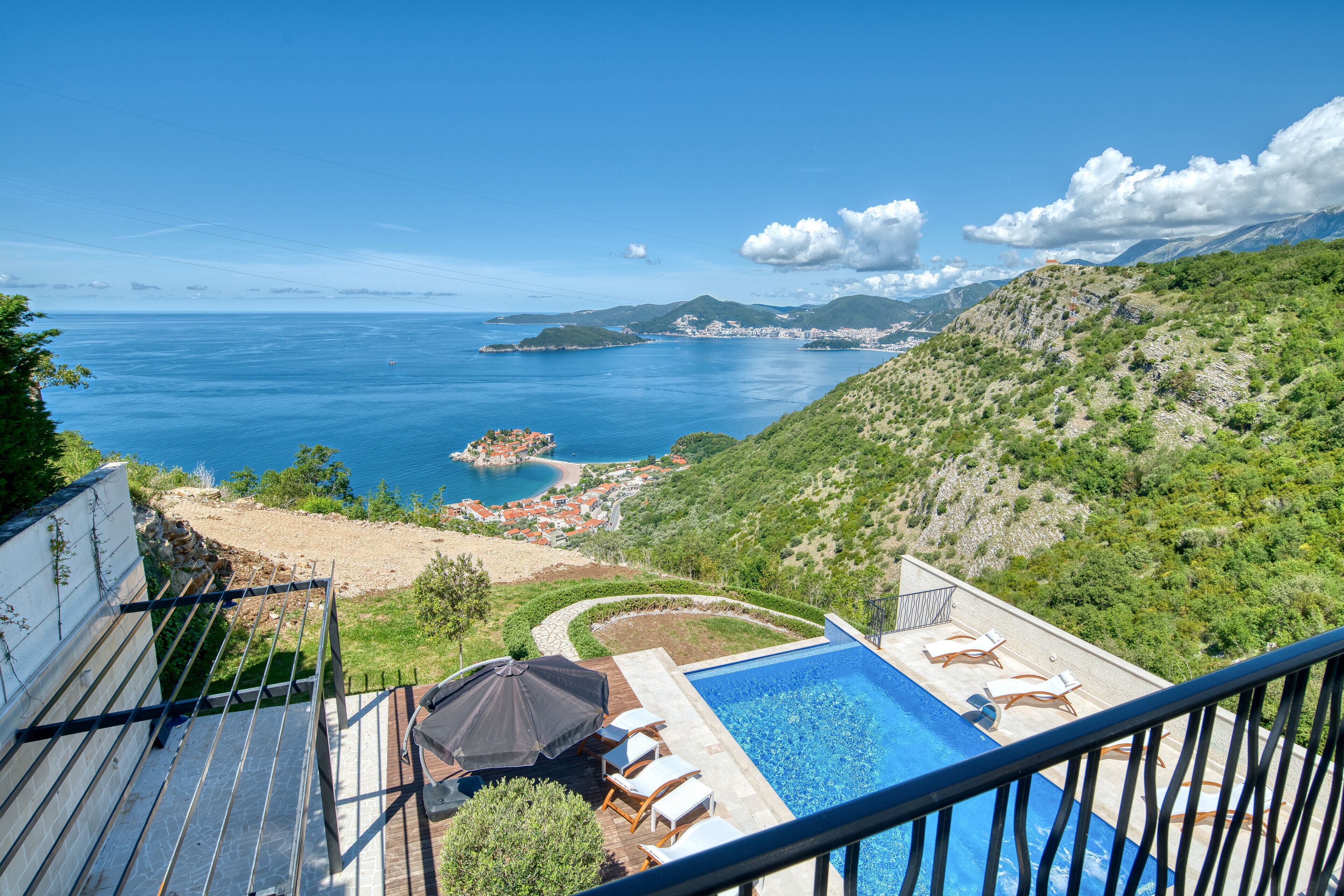 A pool with lounge chairs, a view of the sea, and a mountainous landscape.