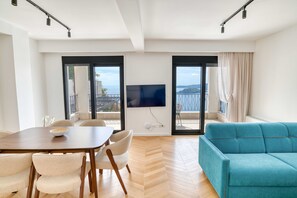 Un saló modern amb zona de menjador, televisió plana penjada a la paret i un sofà.