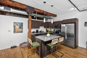 A modern kitchen with dark wooden cabinets, stainless steel appliances, and a central island with chairs. - Top Floor Loft l Downtown Views l Free Parking l Pet Friendly (Des Moines)