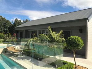 Une maison moderne dotĂ©e dâune piscine, dâune vĂ©randa en verre et dâun patio amĂ©nagĂ© avec du mobilier.