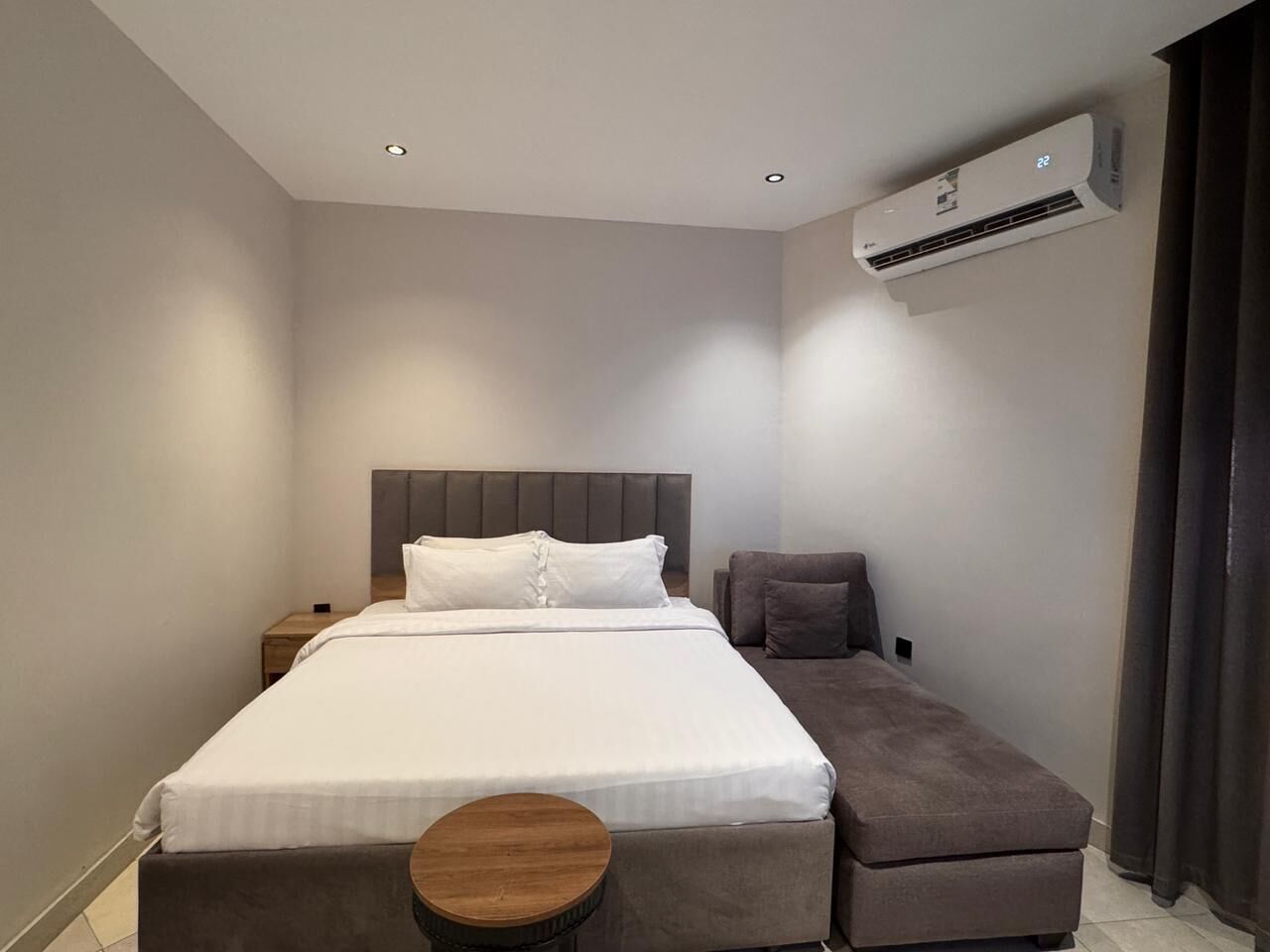 Una habitación de hotel moderna con una cama grande, una mesita de noche, una pequeña mesa redonda, un sofá y un equipo de aire acondicionado.