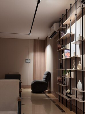 Habitació moderna amb un divà modern fosc, un mur amb panells de fusta, una prestatgeria amb objectes decoratius i un aire condicionat de sostre.