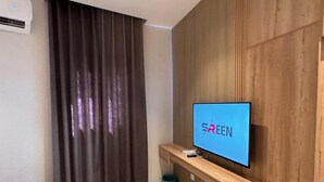 A modern room with a mounted TV on a wooden wall, a curtain, a trash bin, and a sofa. - RAMA Dubai Serviced Apartments 3 Granada (Riyadh)
