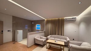 A modern hotel room with a sofa set, a small table, a refrigerator, and a window with curtains. - RAMA Dubai Serviced Apartments 3 Granada (Riyadh)