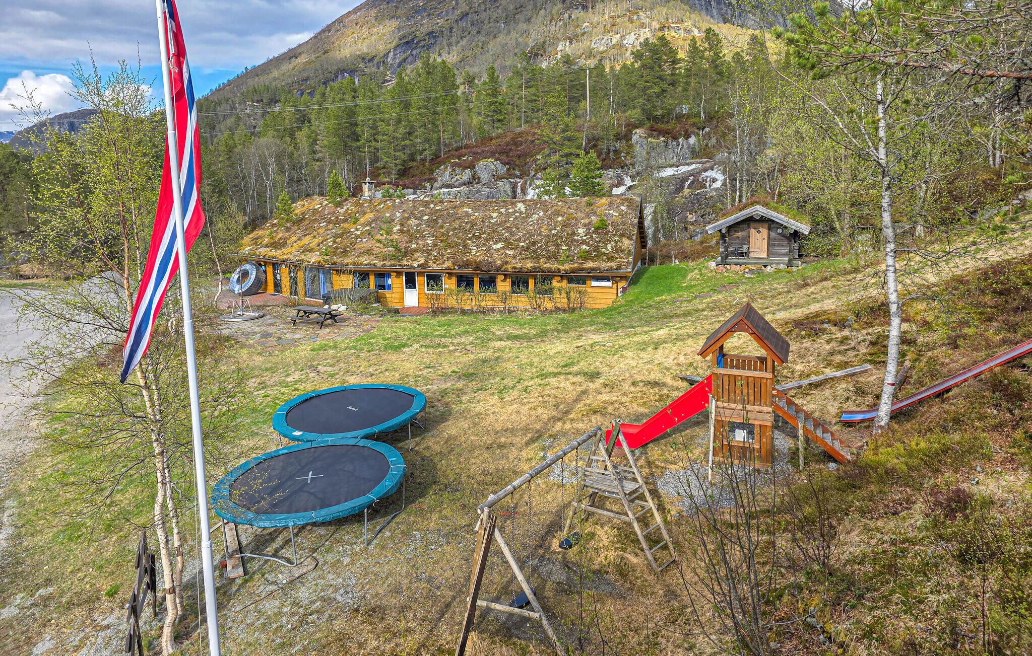 A cabin with a thatched roof, a trampoline, a swing set, and a flagpole.