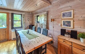 Ein Holzblockhaus-Interieur mit Esstisch, Stühlen, Kamin und gerahmten Bildern an der Wand.