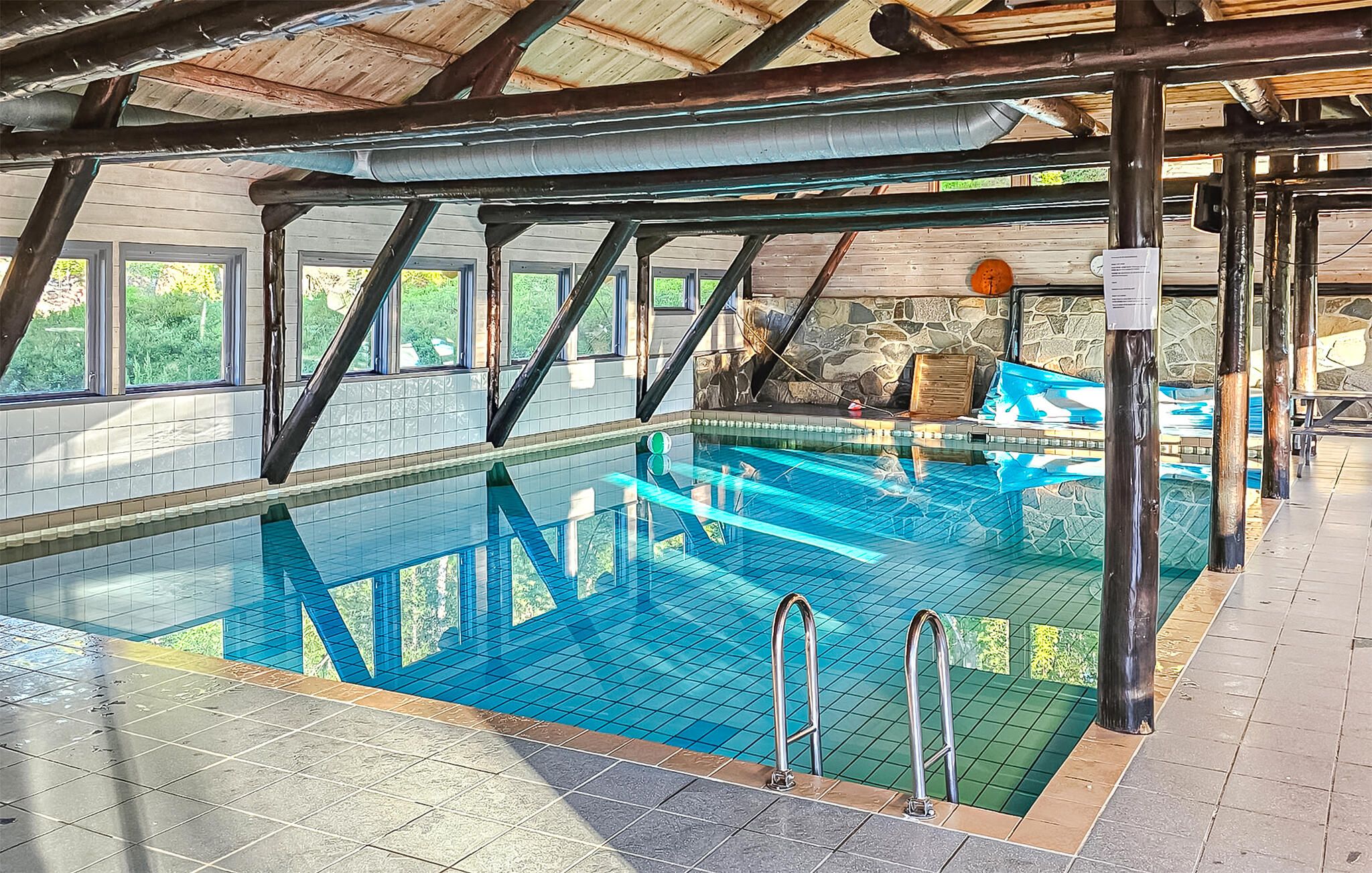 Une piscine intérieure à l’eau claire, entourée de murs en pierre et de poutres en bois.