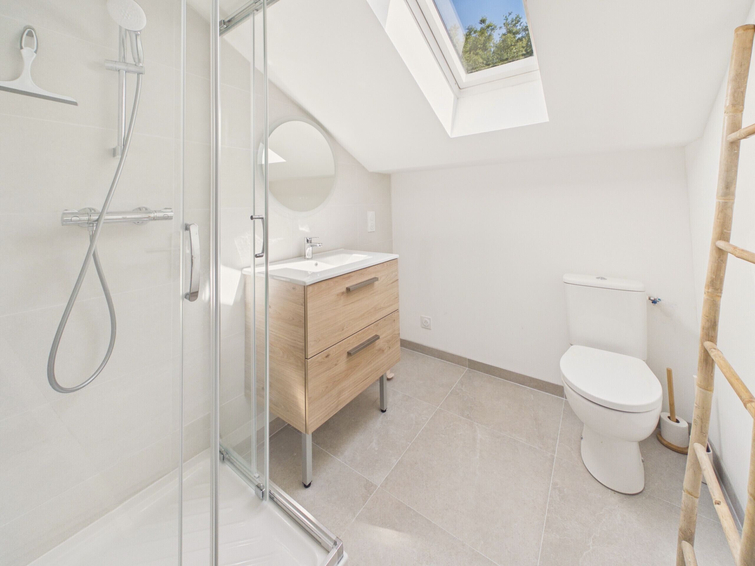 Un baño moderno con cabina de ducha de vidrio, tocador de madera, inodoro y tragaluz.