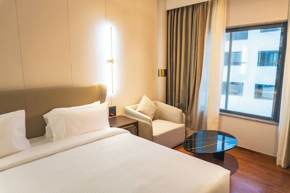 Habitación de hotel con cama, una silla, una mesita y una ventana con cortinas.