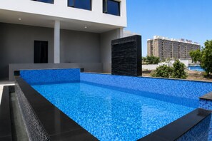 A swimming pool with a blue mosaic tile design, surrounded by a modern building with large windows and a flat roof. - Pride Plaza Indore (Indore)
