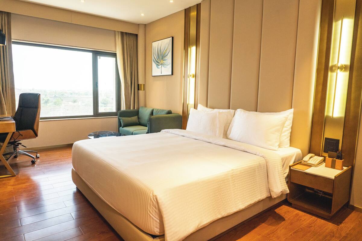 Habitación de hotel con una cama grande, un escritorio, una silla y un ventanal con cortinas.