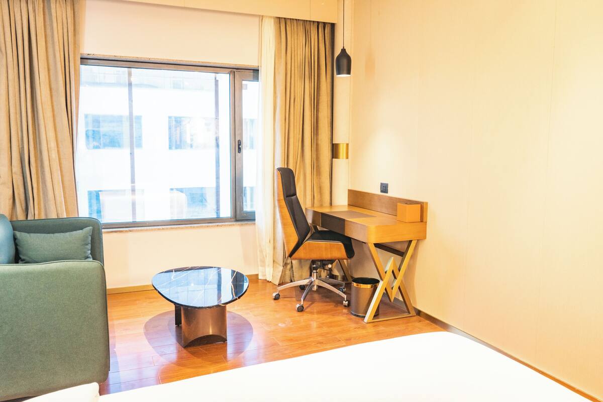 Una habitación de hotel con un ventanal grande, un escritorio, una silla, un sofá y una mesita.