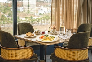Une table à manger avec des assiettes remplies de nourriture, un vase de fleurs et une vue sur le paysage urbain à travers de grandes fenêtres.