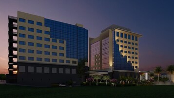 Um hotel moderno com vários andares, grandes janelas e um jardim bem cuidado.