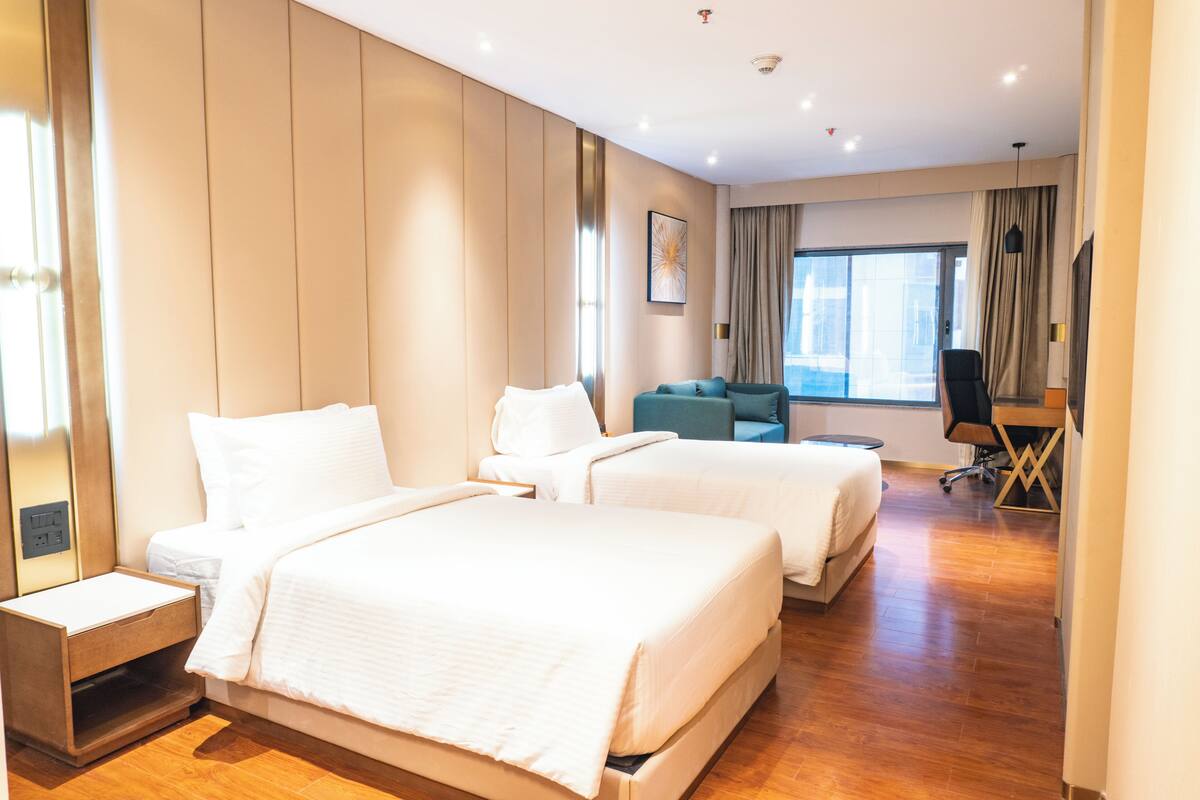 Una habitación de hotel con dos camas, un sofá, un escritorio y un ventanal grande.