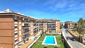 A multi-story residential building with balconies, a swimming pool, and a road in the foreground. - Apartment 'Sancho Go2lloret' with Mountain Views, Wi-Fi, and Air Conditioning (Lloret de Mar)
