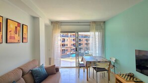 A living room with a sofa, a dining table with chairs, a TV, and a balcony with a view of buildings. - Apartment 'Sancho Go2lloret' with Mountain Views, Wi-Fi, and Air Conditioning (Lloret de Mar)
