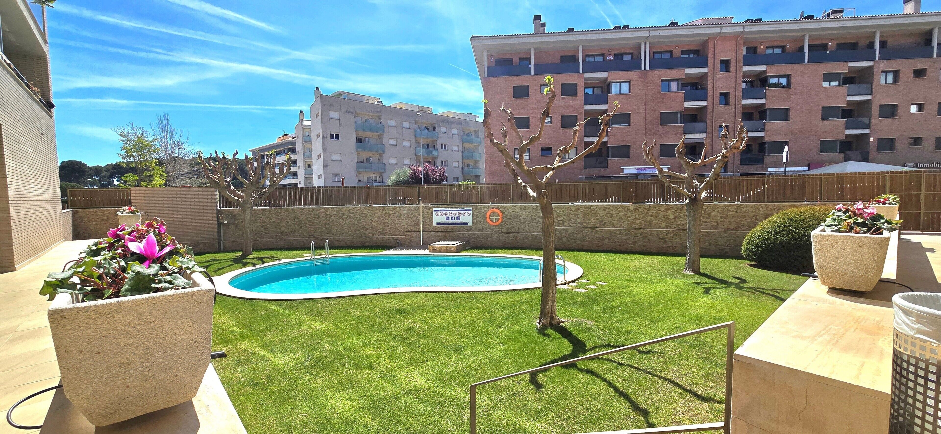 Una piscina, una recinzione in legno e un edificio sullo sfondo con diversi balconi.