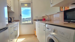 A compact kitchen with a washing machine, a microwave, and a window with a view. - Apartment 'Sancho Go2lloret' with Mountain Views, Wi-Fi, and Air Conditioning (Lloret de Mar)