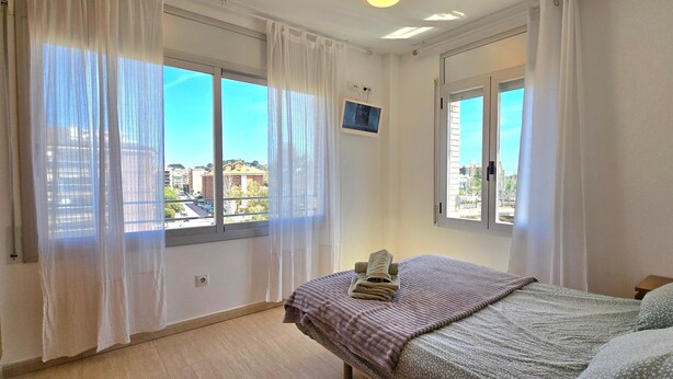 A room with two beds, a window with sheer curtains, a small TV on the wall, and a balcony view. - Apartment 'Sancho Go2lloret' with Mountain Views, Wi-Fi, and Air Conditioning (Lloret de Mar)