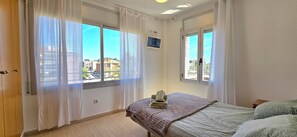 Ein Zimmer mit zwei Betten, einem Fenster mit leichtem Vorhang, einem kleinen Fernseher an der Wand und Balkonblick.