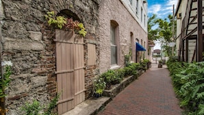 Un étroit sentier pavé de briques, bordé de bâtiments dotés de fenêtres en arc de cercle et surmonté d’un portail en bois.