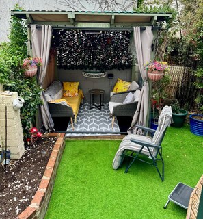 Un'accogliente area esterna con divano e poltrone, immersa nel verde e delimitata da un muro decorativo.