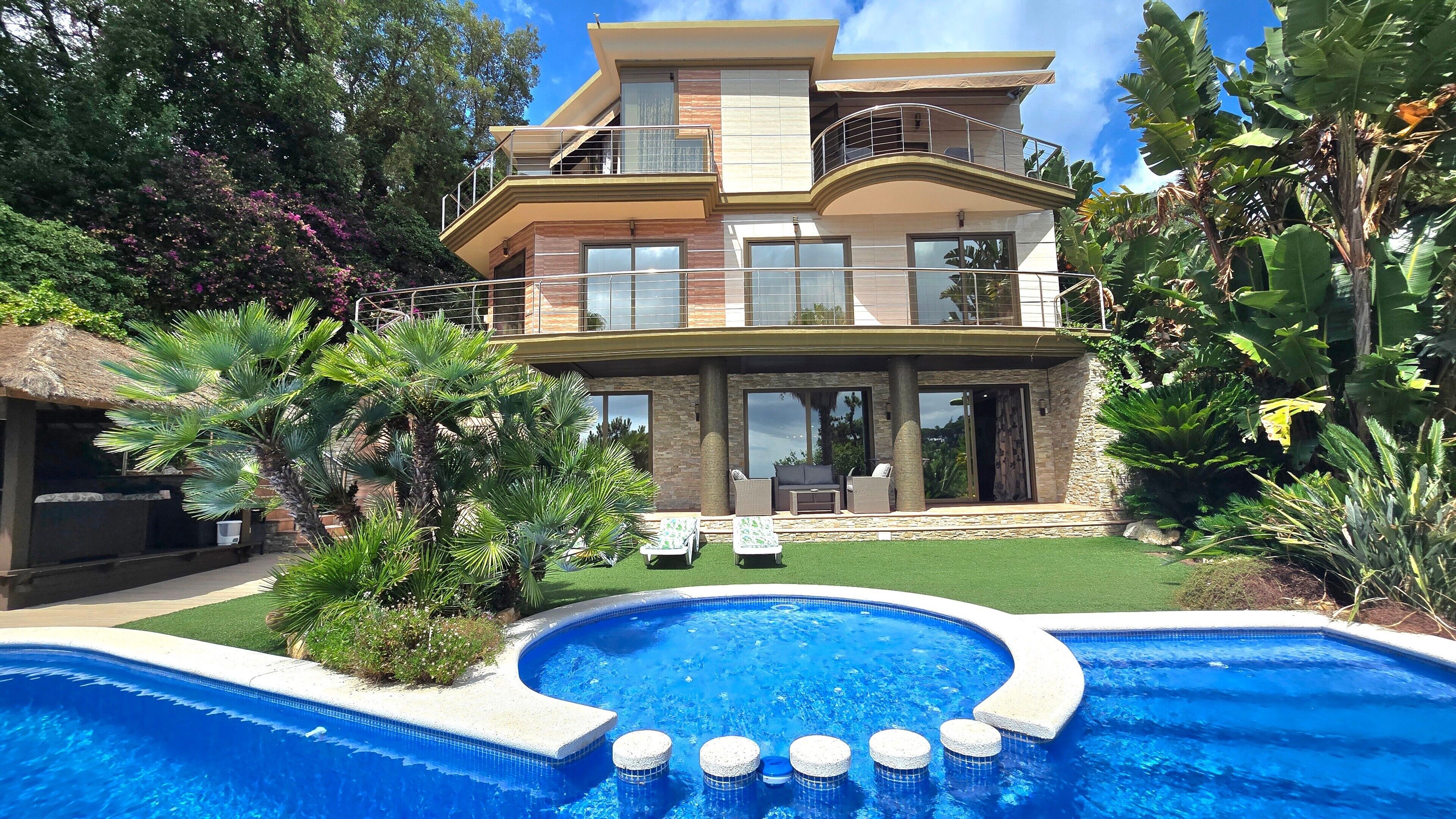 Ein zweigeschossiges Haus mit Swimmingpool, einer Terrasse und Lounge-Möbeln, umgeben von üppiger tropischer Vegetation.