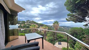 Ein Balkon mit Tisch und Stühlen mit Blick auf eine Hügellandschaft mit Häusern und einem Gewässer.
