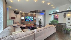Ein modernes Wohnzimmer mit großem Flachbildfernseher, einem Ecksofa, einem Couchtisch und einer Topfpflanze.