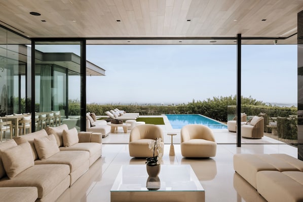 A modern living room with a glass wall, a pool, and outdoor seating. - Villa Bella (West Hollywood)