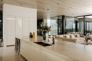 A modern kitchen with a large island, bar stools, a sink, and a potted plant. - Villa Bella (West Hollywood)