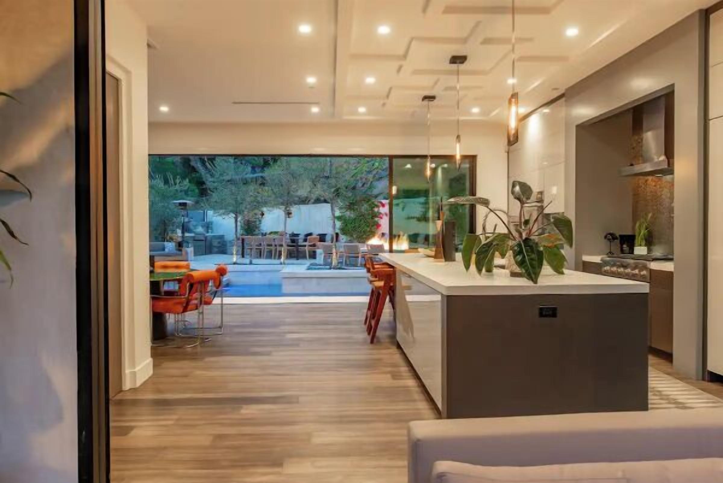 A modern kitchen with a central island, wooden flooring, and a view of an outdoor dining area.