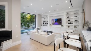 A modern living room with a pool, white furniture, and a TV on the wall. - Gardner Modern (Los Angeles)