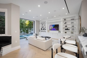 Uma sala de estar moderna com piscina, móveis brancos e TV na parede.