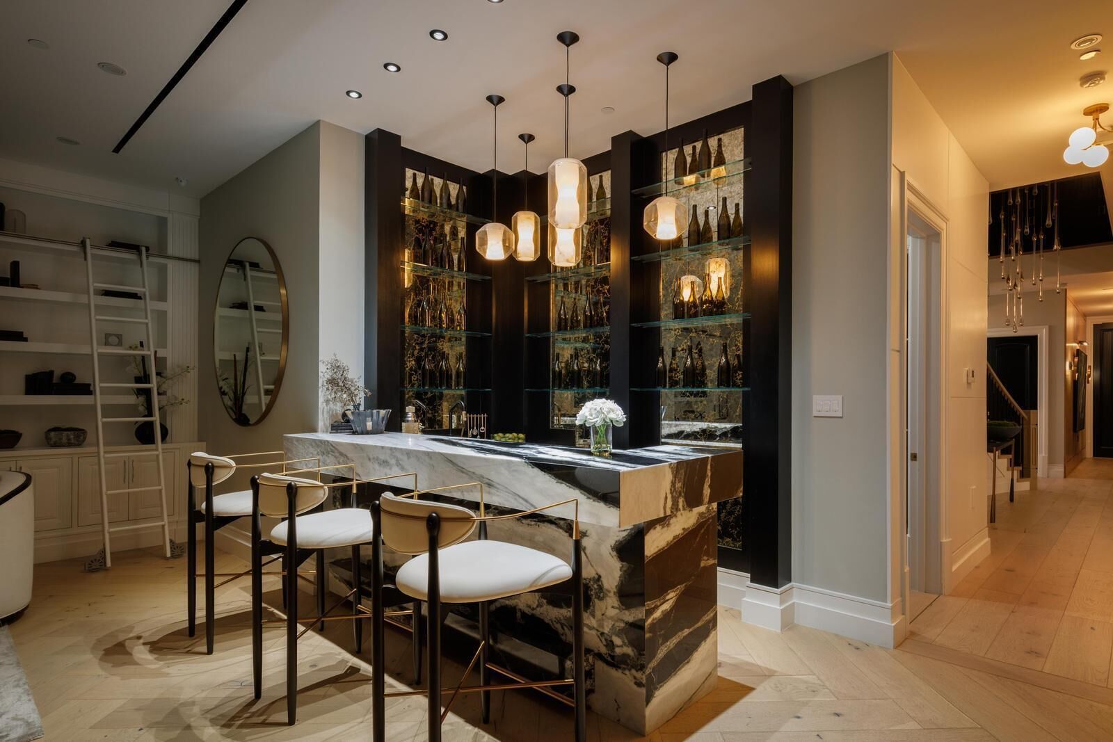 Uma cozinha moderna com ilha de mármore, banquetas, luminárias pendentes e espaço para vinhos.