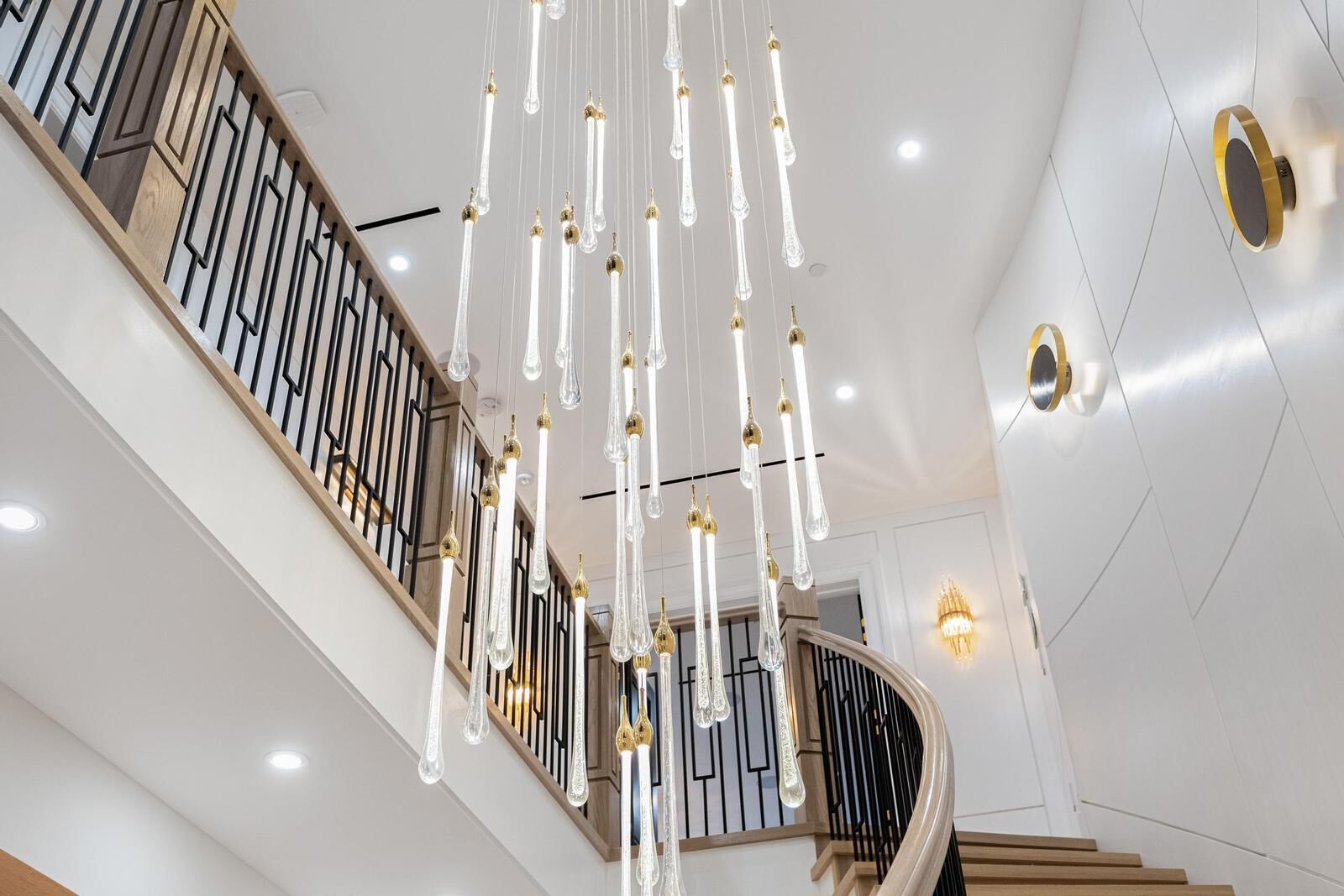 A modern staircase with a wooden railing and hanging crystal light fixtures.