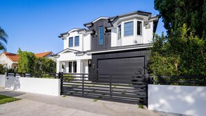 A modern two-story house with a large garage door, a gated driveway, and a well-maintained lawn. - Gardner Modern (Los Angeles)