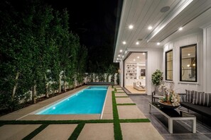 A modern outdoor pool area with a built-in seating area and a well-lit interior space. - Gardner Modern (Los Angeles)