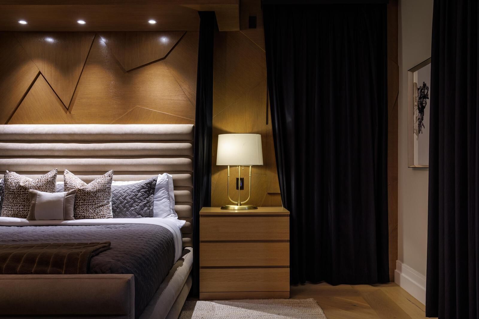 Un dormitorio moderno con cama, mesita de noche, lámpara y cortinas oscuras.