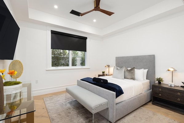 Um quarto moderno com uma cama grande, mesas de cabeceira, um banquinho e um ventilador de teto.