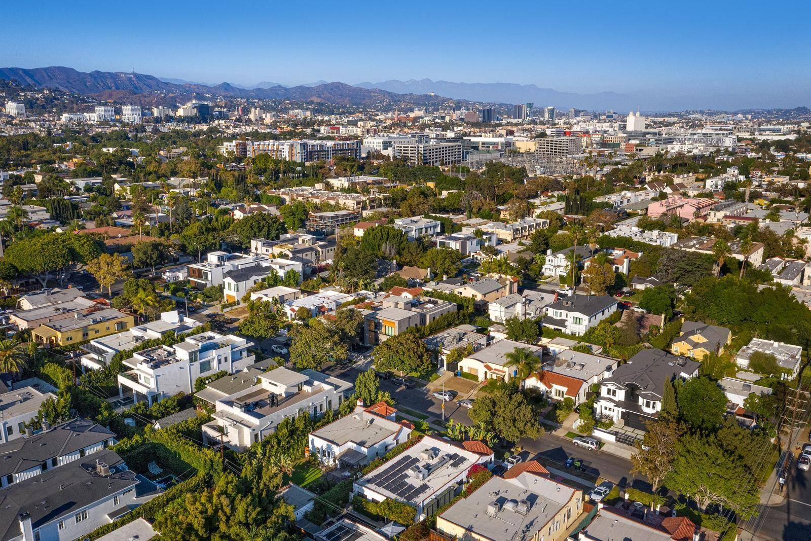 Zona residencial con casas unifamiliares y edificios de apartamentos, rodeada de vegetación y montañas al fondo.