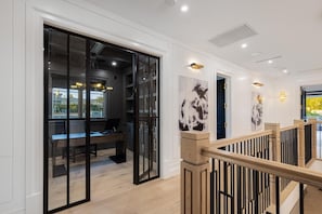 A modern interior with a glass door leading to a workspace, a staircase with wooden railings, and artwork on the walls. - Gardner Modern (Los Angeles)