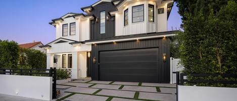 A two-story house with a large garage door, a covered driveway, and a well-maintained lawn.