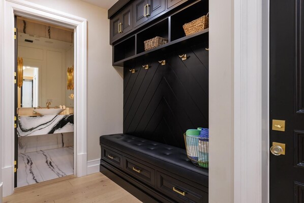 A modern bathroom with a marble vanity, a black bench with drawers, and a black shelving unit with baskets. - Gardner Modern (Los Angeles)