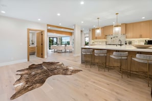 A modern kitchen with wooden cabinets, a central island with bar stools, and pendant lighting. - Sea Vista (Malibu)