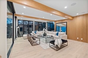 Un salón moderno con un sofá blanco, una mesa de centro de vidrio y una pared de acento de madera.