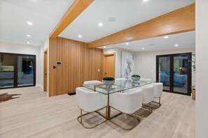 Un comedor moderno con una mesa de vidrio y sillas blancas, paneles de madera y vista a una piscina.