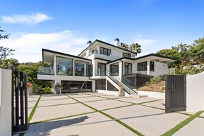 A modern two-story house with a spacious patio, a staircase, and a gated entrance.
