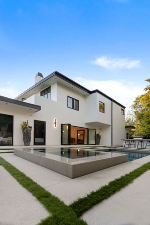 Una casa moderna de dos pisos con piscina, ventanas amplias y césped cuidado.